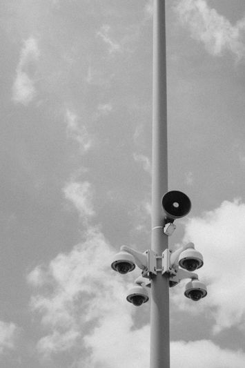 cuatro cámaras blancas y un megáfono dentro de un alto poste blanco contra el cielo