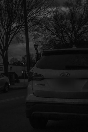 A black and white image of a parked Hyundai SUV on a street at night, with bare trees and a lamppost in the background.