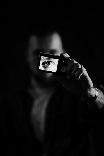 Person holding a camera displaying an eye on its screen, set against a dark background.