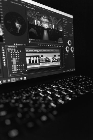 Black and white image of a laptop screen displaying video editing software, with keyboard in the foreground.