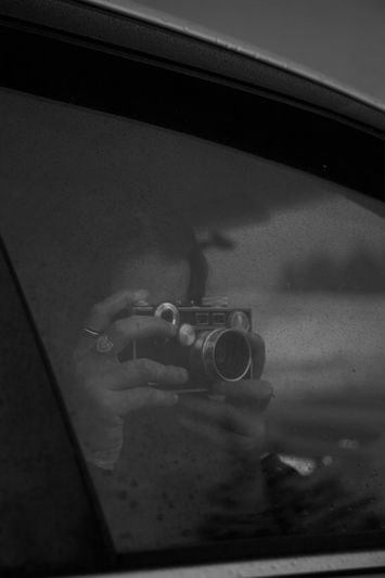 foto en blanco y negro de una mujer tomando una foto desde el interior de un coche con la ventana cerrada