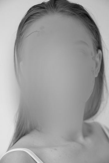 an anonymized face of a female model in a white tank top, black-and-white photo