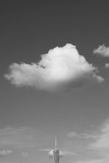 Un nuage léger flotte dans un ciel clair au-dessus du sommet d'une haute tour. L'image est en noir et blanc.