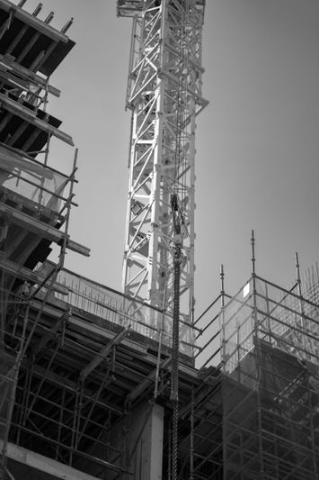 Image en noir et blanc d’un chantier de construction avec des échafaudages et une grande grue sur fond de ciel dégagé.