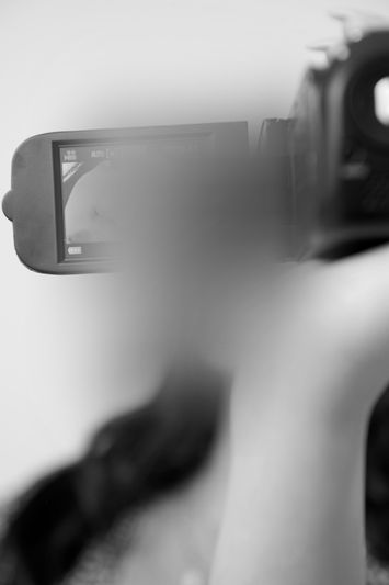 Une personne tient une caméra vidéo et se concentre sur l'écran. Le visage est flou, avec une palette de couleurs monochrome.
