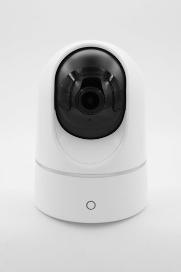 White security camera with a black lens, mounted on a sleek, modern base, standing against a plain white background.