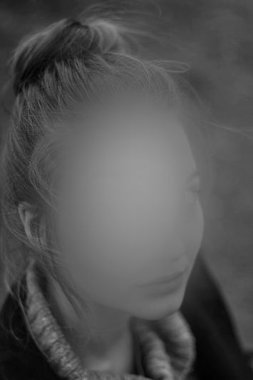 Fotografía en blanco y negro de una mujer con el rostro borroso, vestida con un jersey y una chaqueta, y con el pelo recogido en un moño.