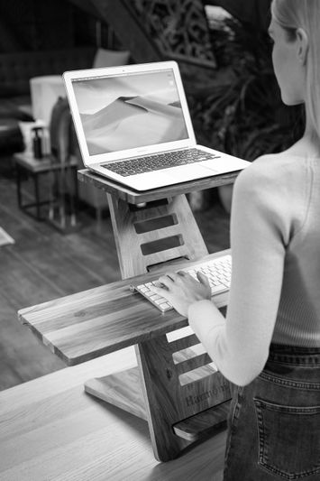 Une personne utilise un bureau debout en bois avec un ordinateur portable et un clavier. L'écran affiche un paysage désertique.