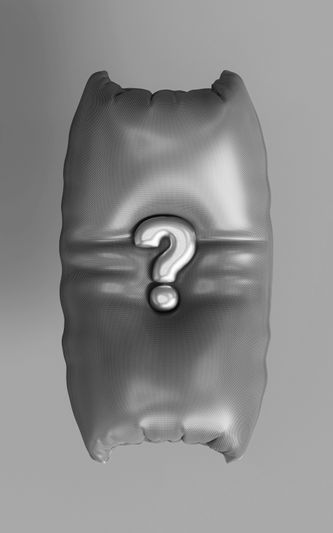 Silbernes Kissen mit spitzen Ecken und einem geprägten Fragezeichen in der Mitte, vor einem einfarbigen grauen Hintergrund.