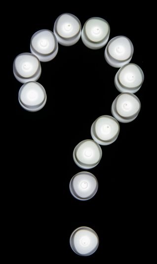Des bougies blanches disposées en forme de point d'interrogation sur un fond noir.