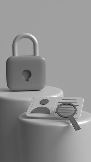 Image en niveaux de gris d'un cadenas et d'une loupe sur une carte d'identité sur des socles cylindriques, symbolisant la sécurité et la vérification d'identité.