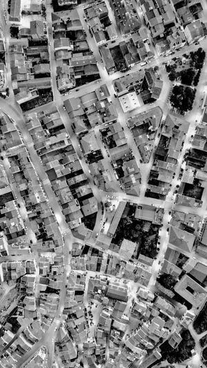 Vue aérienne d'une zone urbaine densément peuplée avec des rues étroites, des bâtiments serrés et de la verdure dispersée en noir et blanc.