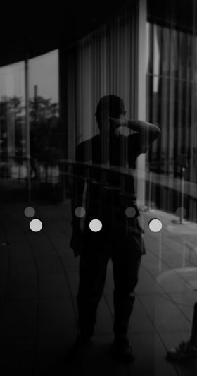 Silueta de una persona reflejada en una ventana de vidrio, con pegatinas circulares visibles y un paisaje urbano de fondo.