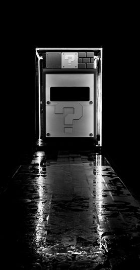 Un couloir faiblement éclairé menant à une grande boîte illuminée avec un point d'interrogation, ressemblant à une boîte mystère d'un jeu vidéo.