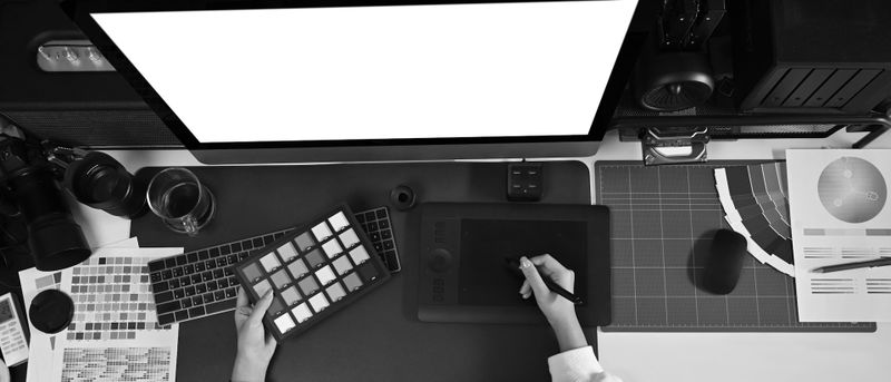 An overhead view of a workspace with a digital drawing tablet, keyboard, grid mat, and various design tools.