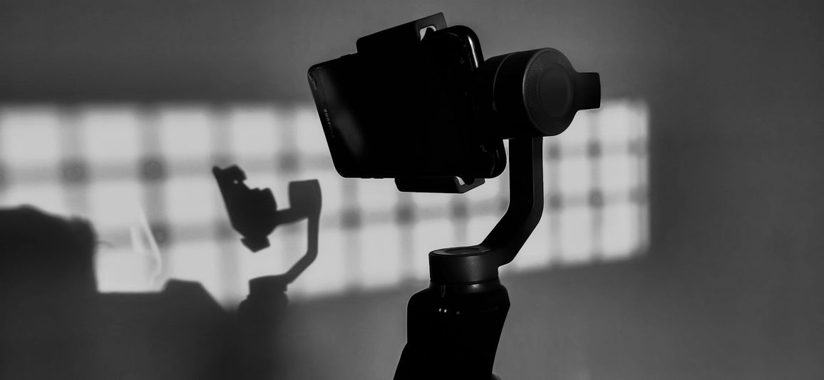 La silueta de una cámara en un gimbal con su sombra proyectada en una pared, iluminada por una fuente de luz con patrón de cuadrícula.