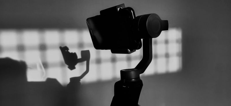 A silhouette of a camera on a gimbal with its shadow cast on a wall, illuminated by a grid-patterned light source.