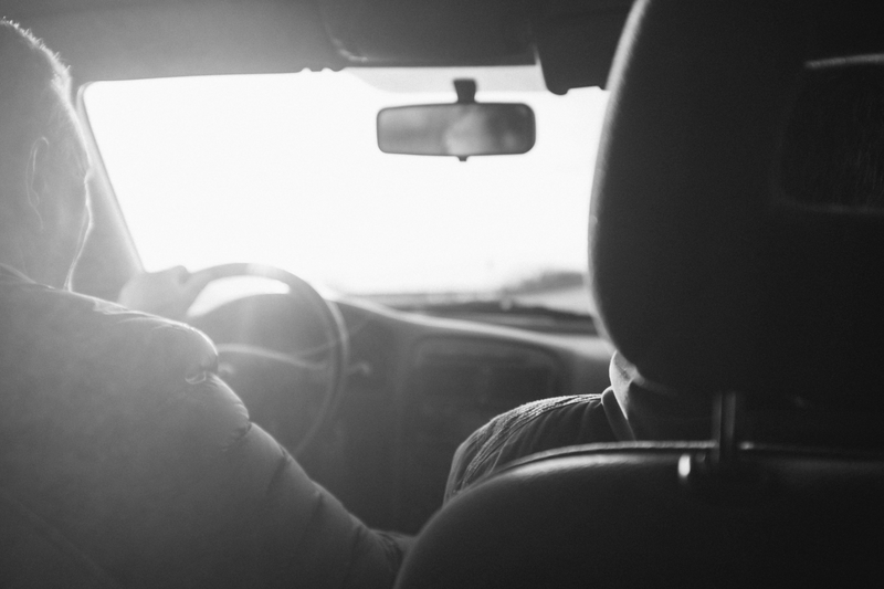 Fotografía en blanco y negro de una persona conduciendo un automóvil, con la luz del sol entrando por el parabrisas, resaltando el interior.