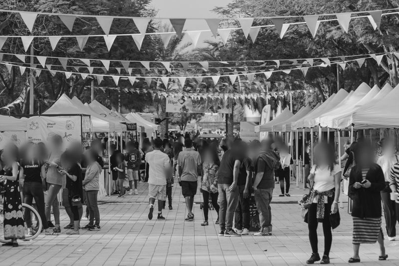 A bustling outdoor market with people walking between rows of tents, adorned with triangular flags hanging overhead.