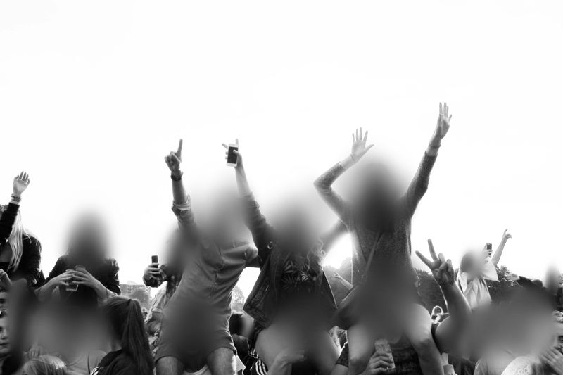 Crowd at an outdoor event, with blurred faces, raising hands and phones in the air, creating a lively and energetic atmosphere.