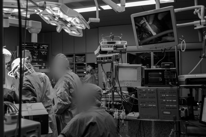 A black and white photo of a busy operating room with surgeons, medical equipment, and a monitor displaying a surgical procedure.