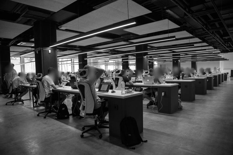 Black and white image of a spacious, modern office with rows of people working at desks equipped with computers and chairs.