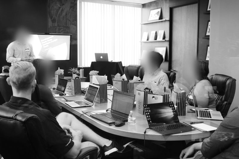 Person at desk with multiple monitors displaying blurred video call participants, notebooks, keyboard, and a calculator on the desk.