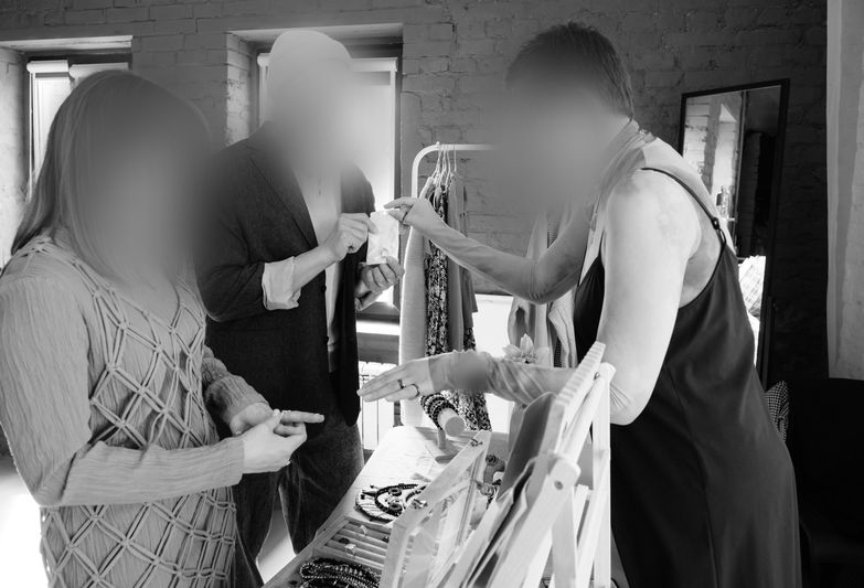 Trois personnes examinent des bijoux exposés sur une table dans une pièce bien éclairée aux murs en briques.