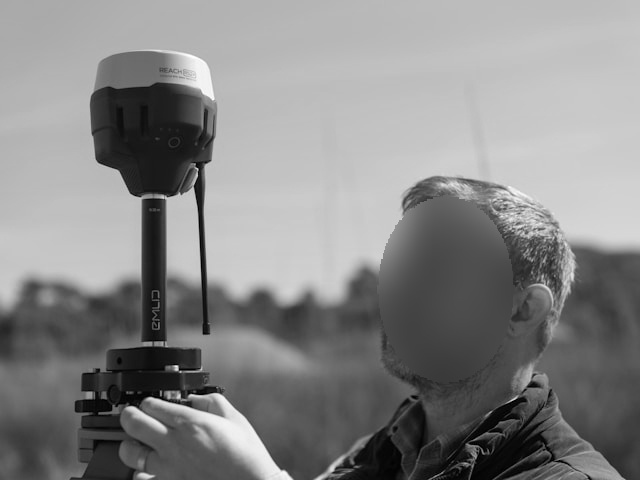 DSGVO Artikel 25: Eine Person hält im Freien Vermessungsgeräte und blickt nach oben. Der Hintergrund ist unscharf und zeigt Bäume und einen klaren Himmel.