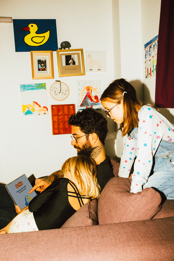 Vater sitzt mit seinen zwei Töchtern auf dem Sofa, alle schauen gemeinsam auf ein iPad mit dem hiToco-Startbildschirm.
