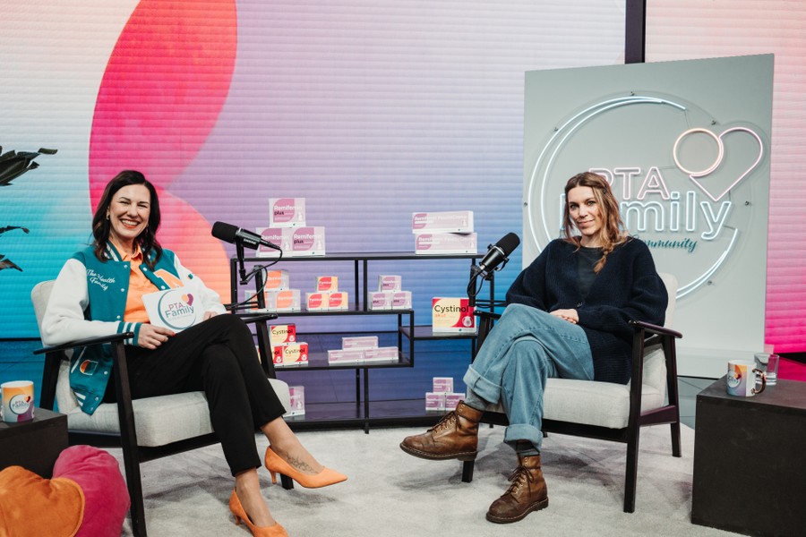 PTA Family Podcast von PTA zu PTA. Two women sit in armchairs with microphones, smiling during an interview on a set with colorful decor and products on display.