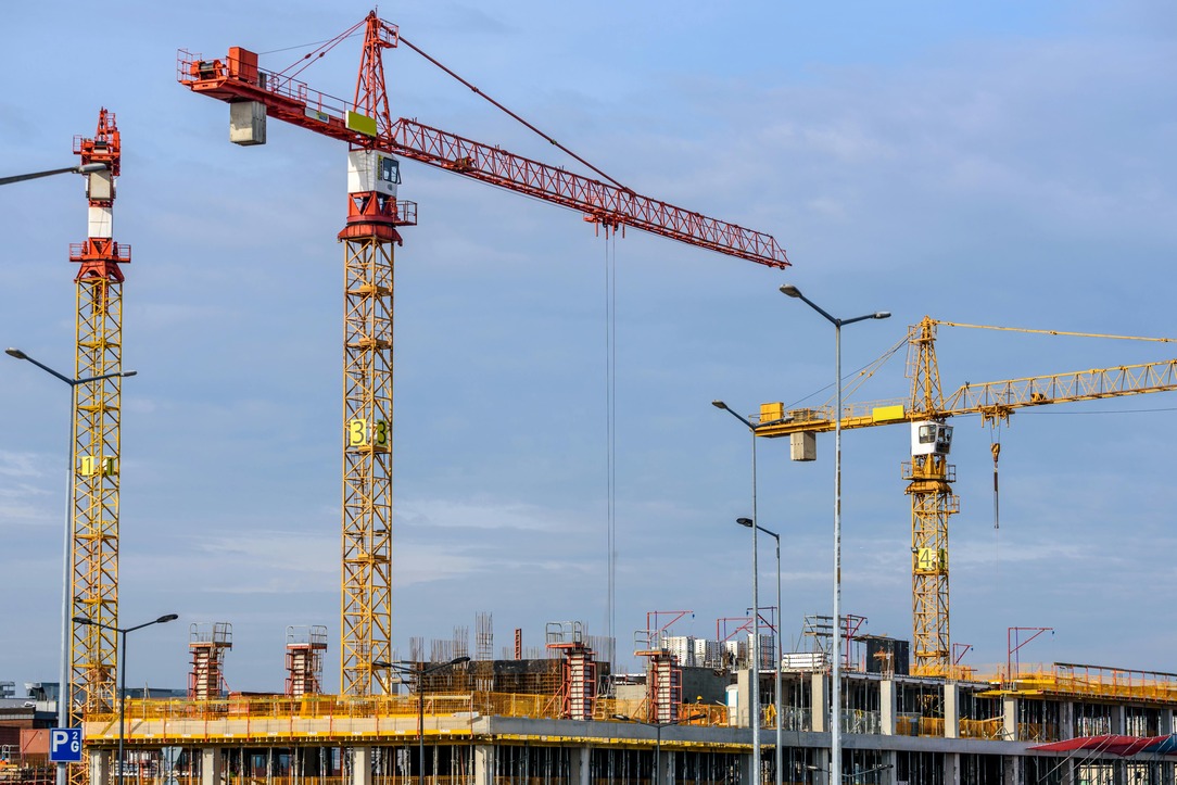 Multiple cranes at a construction site with a partially built structure and clear blue sky in the background.