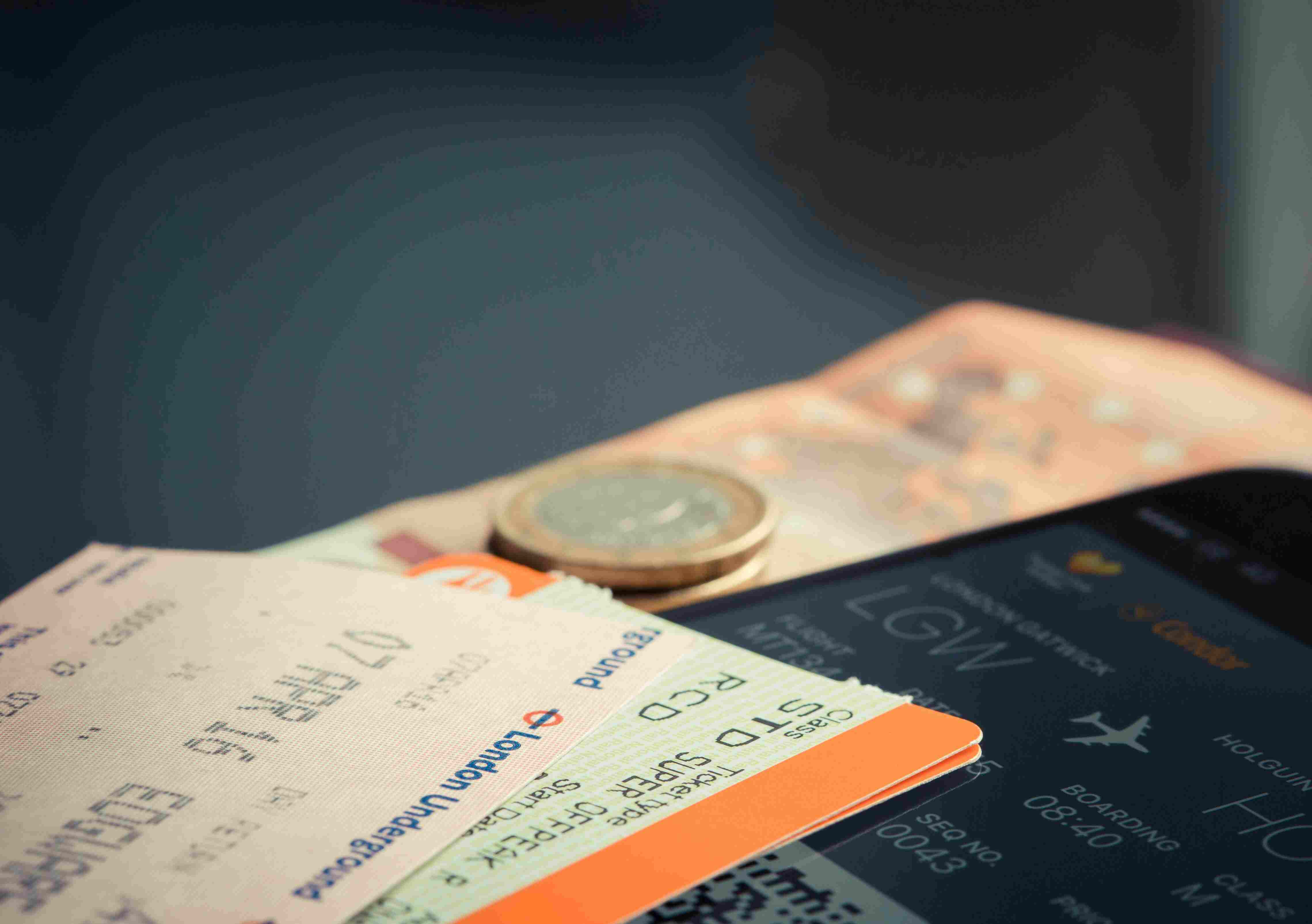 Close-up of travel documents including boarding passes, a smartphone displaying flight details, banknotes, and coins on a surface.