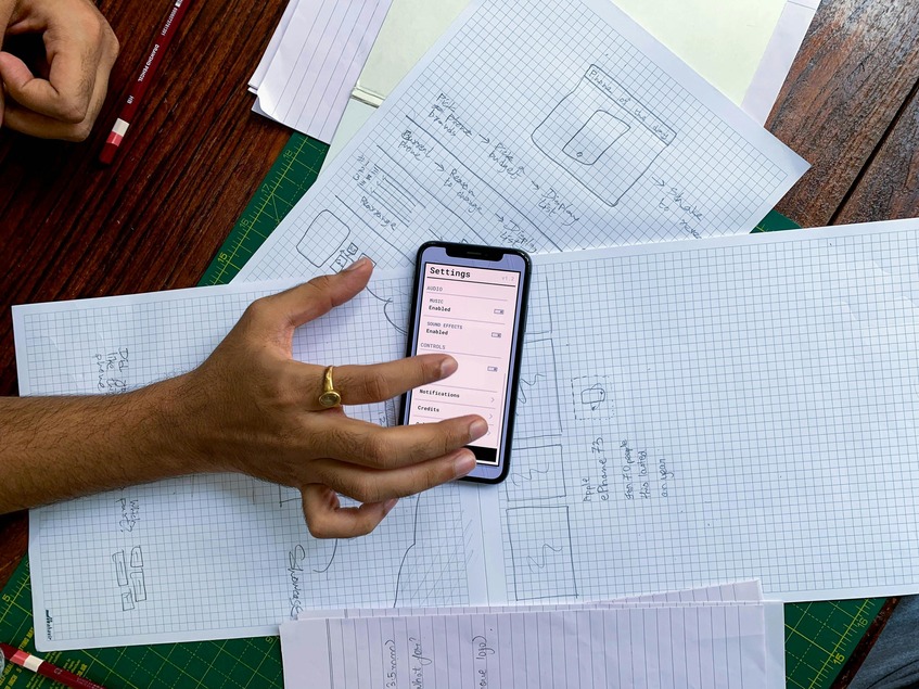 Person holding a smartphone over graph paper sketches and notes, possibly planning a design or layout.