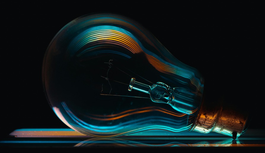Close-up of a light bulb laying on its side, illuminated with vibrant blue and orange reflections against a dark background.