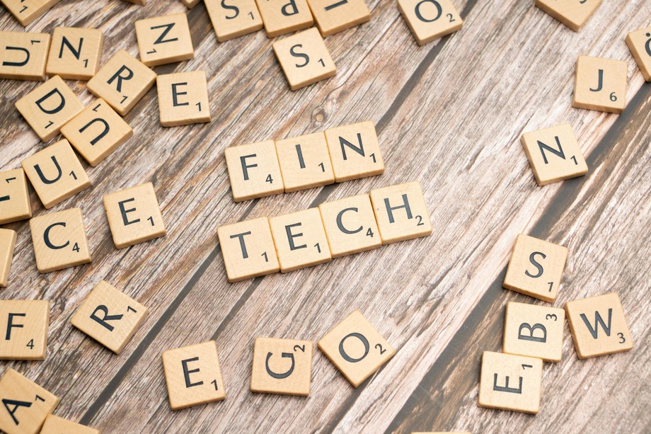 Scrabble tiles spelling "Fintech" on a wooden surface, surrounded by scattered letter tiles.