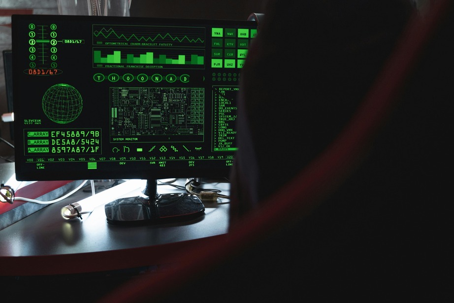 A computer monitor displaying green digital data and graphs in a dimly lit room, suggesting a tech or cybersecurity setting.