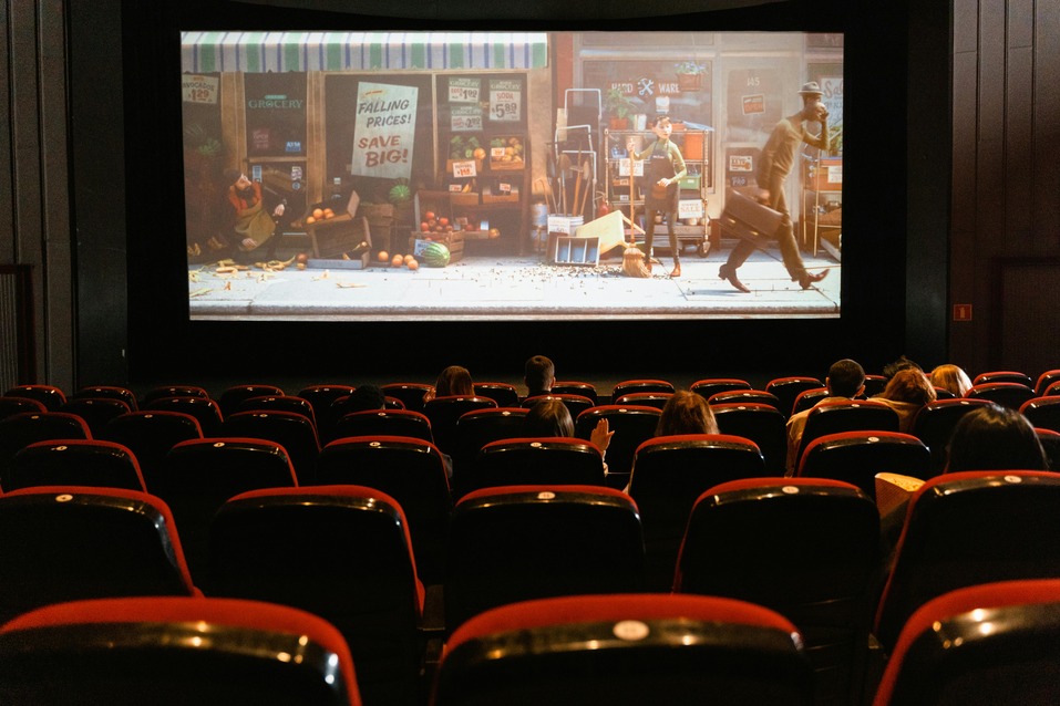 Interior of a movie theatre with rows of red seats facing a large blank screen, soft aisle lighting along the steps, and a darkened atmosphere ready for a film screening.
