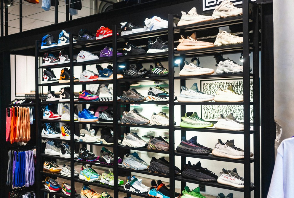 Display of various sneakers in a store, arranged on black shelves, with a range of colors and styles visible.