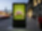 Ein City-Light-Poster mitten in der Stadt auf einer belebten Einkaufspromenade zeigt einen superkleinen Parfumflakon mit einer riesig wirkenden Ballpumpe in Altrosa.  Headline: „Ein Bisschen vom Besten“. Darunter steht: „Stickado von Aoste – in sechs leckeren Sorten.“ Daneben ist der Packshot einer Tüte Stickado zu sehen.   Die Farbe des Hintergrunds ist leuchtend Grün, genau wie die Tüte.