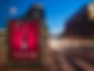 Ein City-Light-Poster mitten in der Stadt an einer belebten Straße zeigt eine superkleine, aber feine Weinflasche, die mit einem normalgroßen Korkenzieher entkorkt wird. Headline: „Ein Bisschen vom Besten“. Darunter steht: „Stickado von Aoste – in sechs leckeren Sorten.“ Daneben ist der Packshot einer Tüte Stickado zu sehen. Die Farbe des Hintergrunds ist bordeaux, genau wie die Tüte.