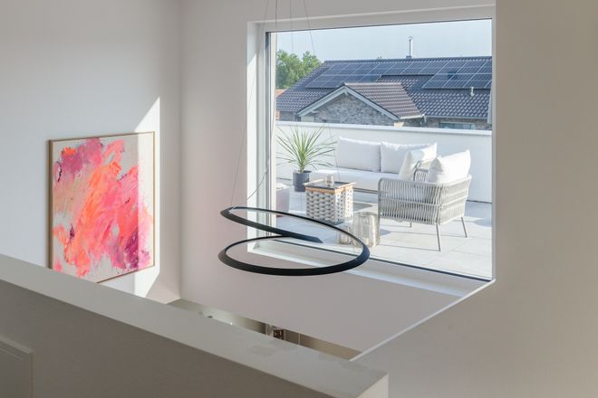 Modern white interior with abstract pink artwork, large window showing a rooftop patio with seating and plants, and a sleek black pendant light.