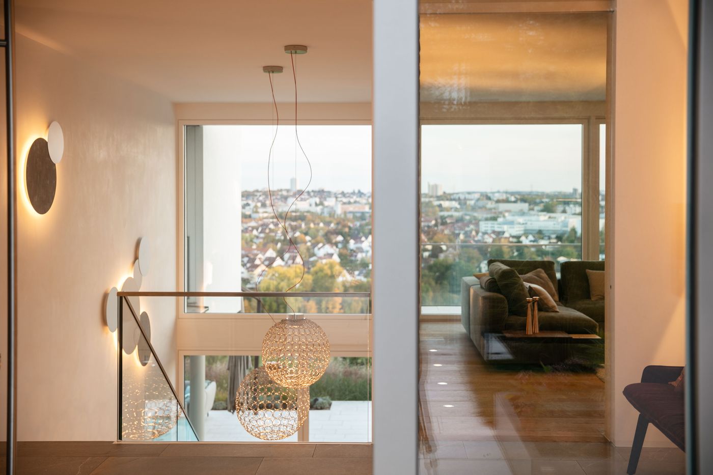 Modern interior featuring a staircase with decorative lighting and a glass wall overlooking a cityscape, leading to a cozy living area.