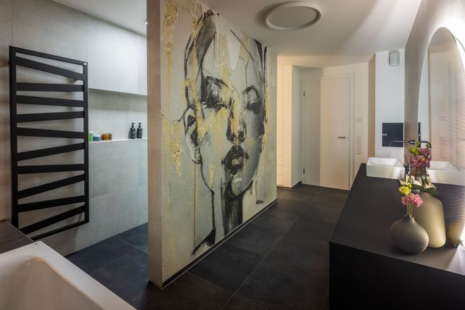Modern bathroom with large mural of a woman's face on the wall, sleek black fixtures, dual sinks, and decorative vases with flowers.