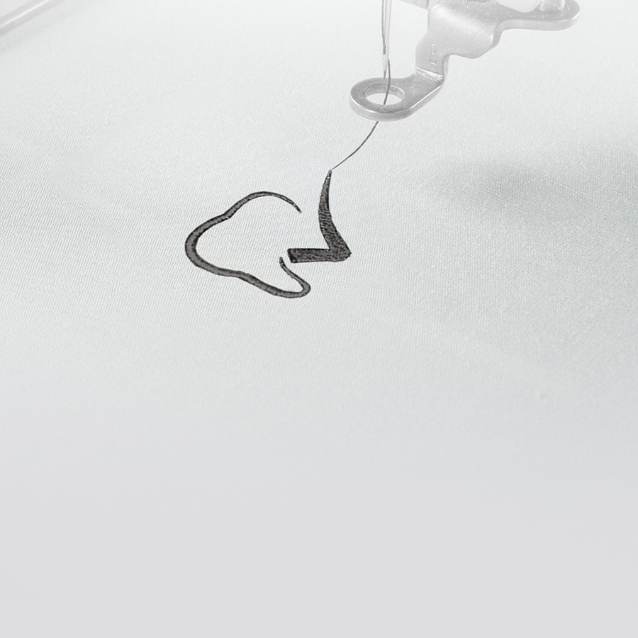 Eine Stickkopf während der Stickung eines der Standardlogos von 7days, welches einen Zahn mit einem Haken zeigt. Daneben ein Haufen verschiedener Stickmotive