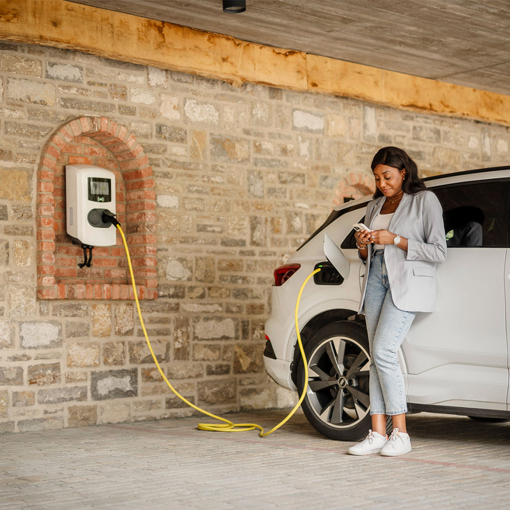 Frau lehnt an E-Auto an Ladestation