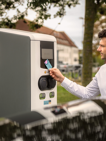 Mann haelt Ladekarte an Ladestation