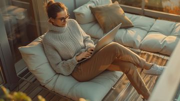 Frau sitzt am Laptop auf ihrem Balkon in der Sonne