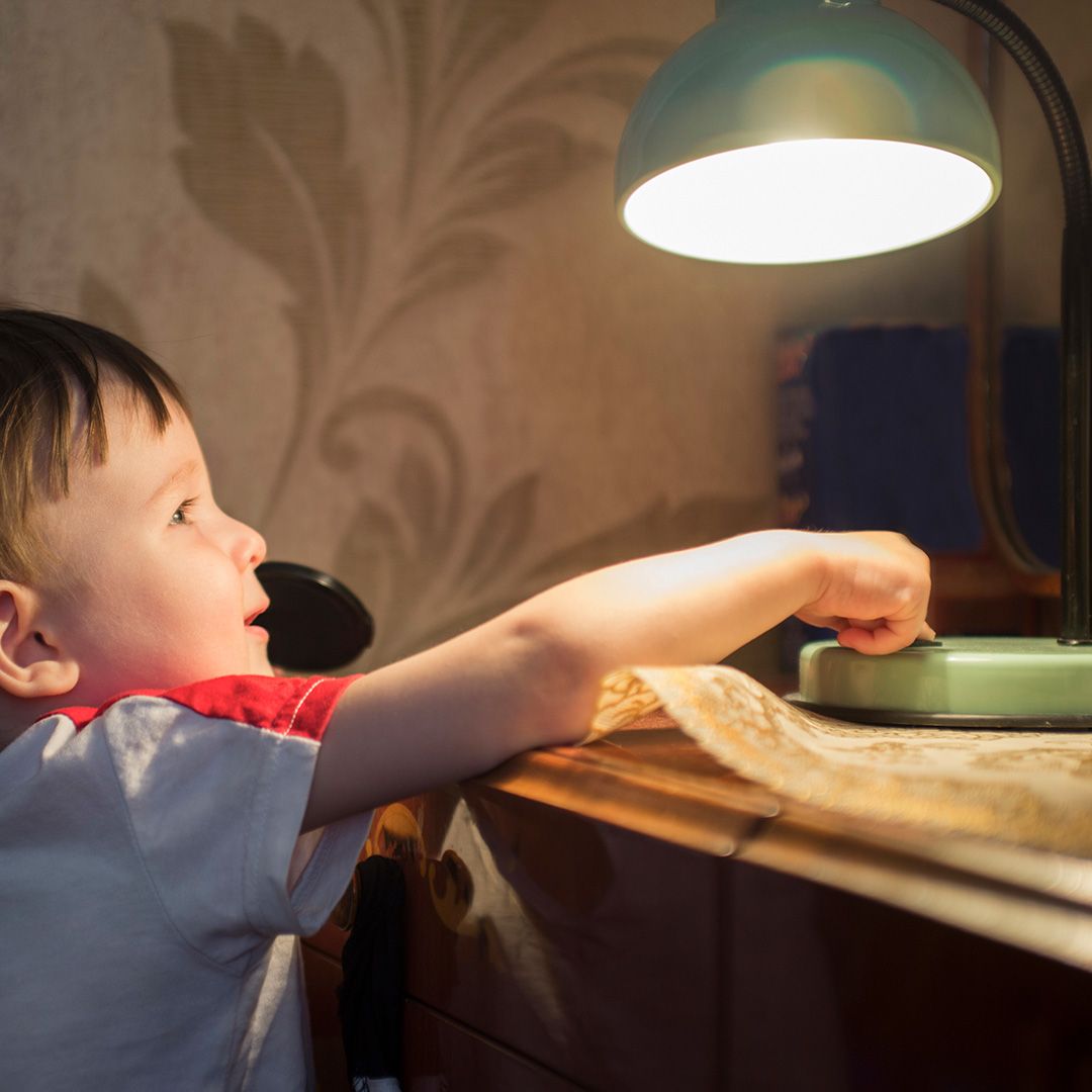 Kind drueckt auf den Knopf einer Lampe