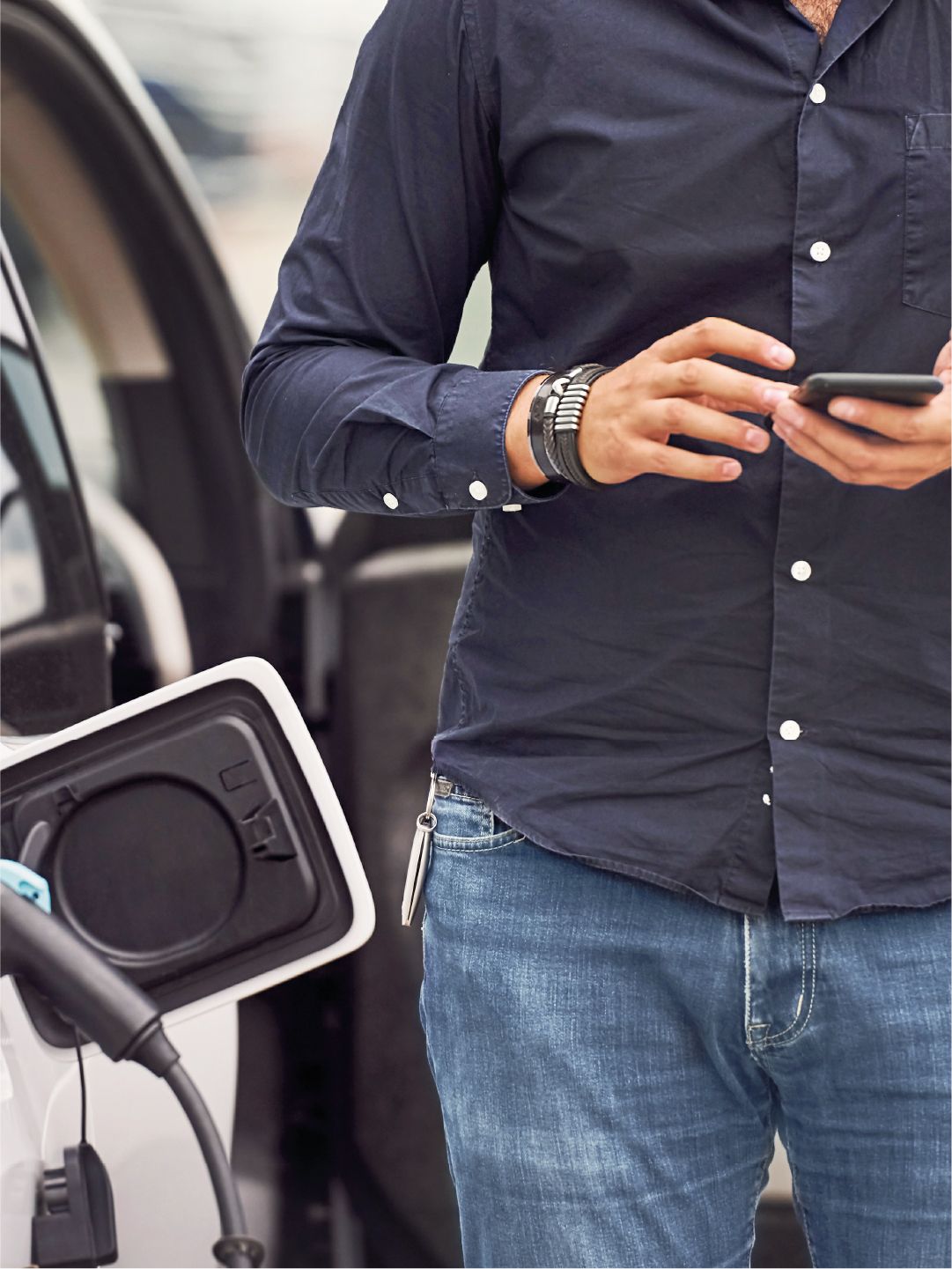 Mann checkt sein Handy, während sein E-Auto lädt